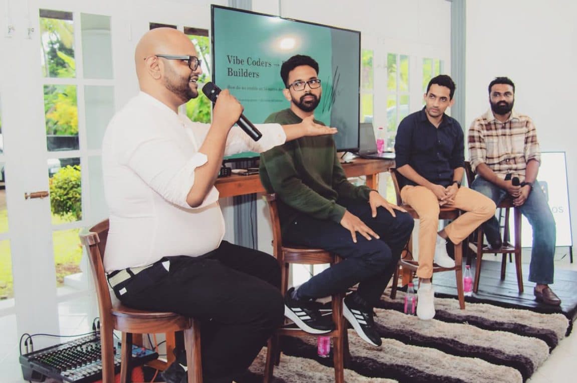 A four-person founder panel on stools, one speaking into a microphone